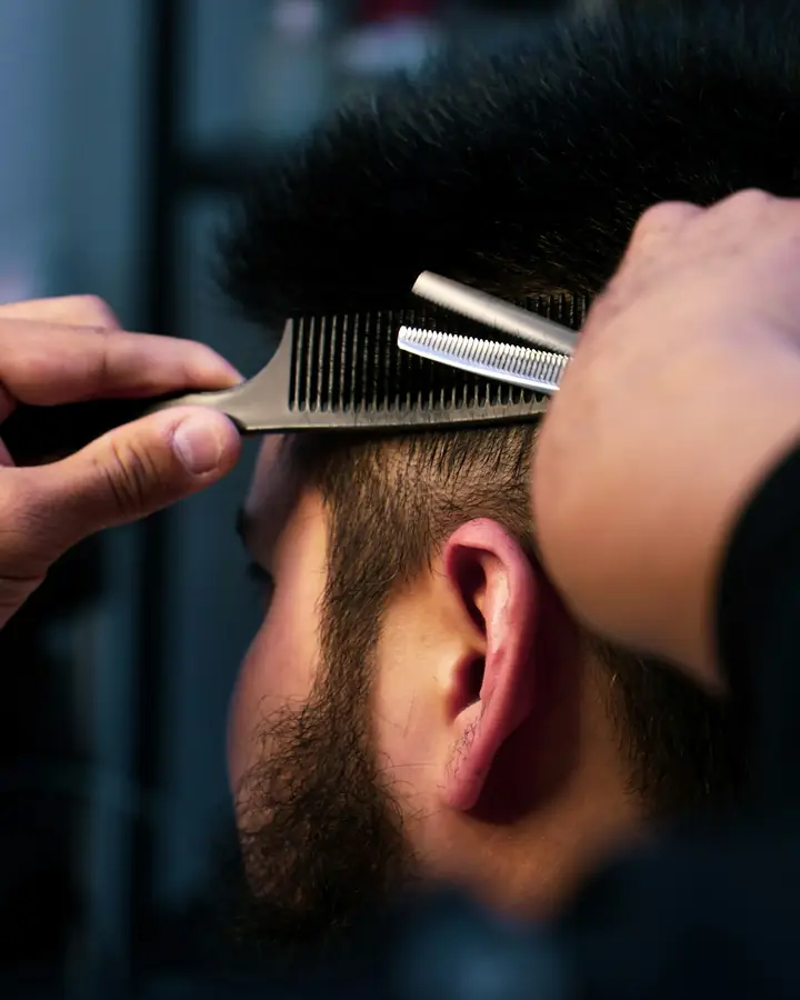 Kapster memotong rambut pelanggan dengan sisir dan gunting penipis.
