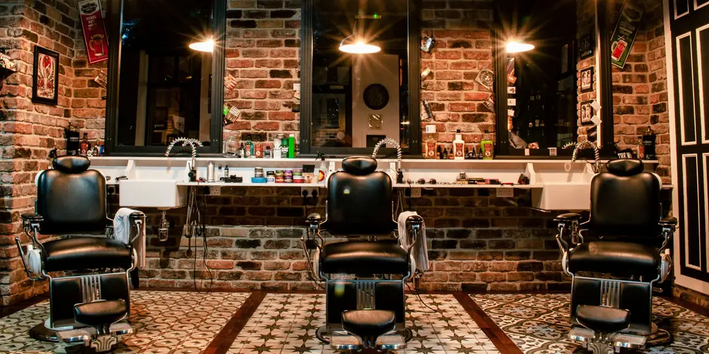 Tiga kursi barber di depan cermin dan dinding bata.